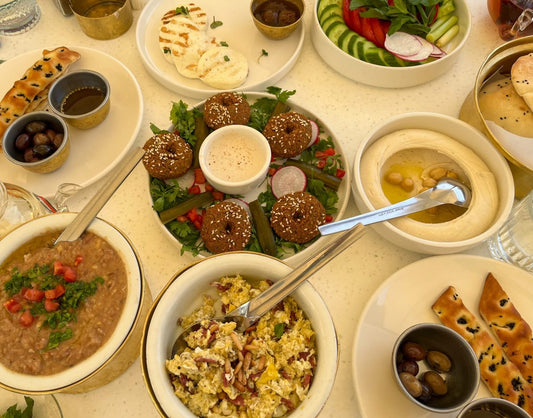 An overhead photo of various Arabic breakfast dishes including falafel with tahini sauce, scrambled eggs, ful mudammas, hummus, halloumi cheese and olives.