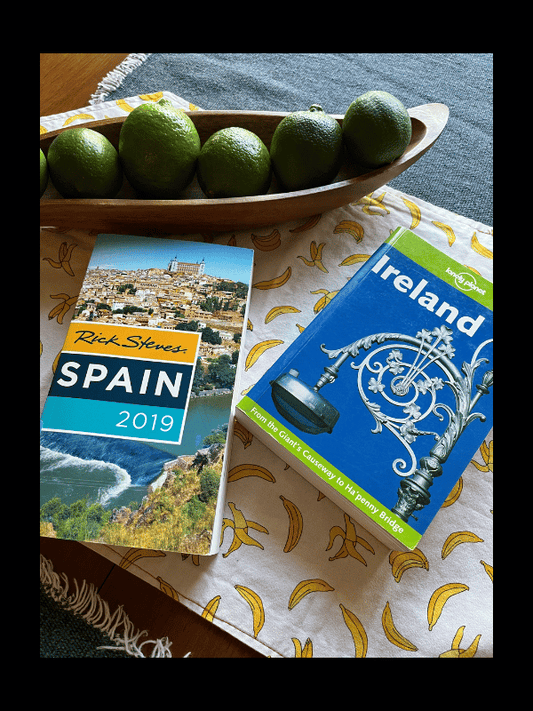 Photo of 2 travel guides on a tabletop: one for Spain, one for Ireland. At top of photo is a wooden dish with limes.